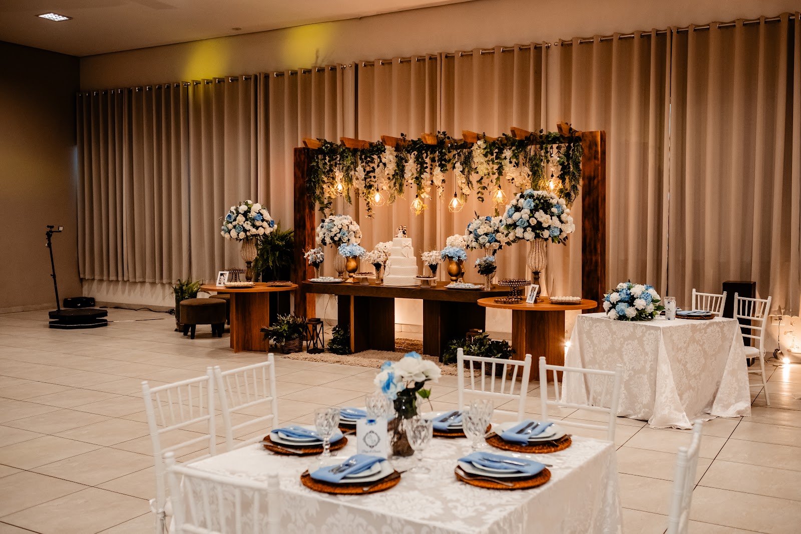 Salão decorado com painel de flores, cortinas iluminadas e mesas