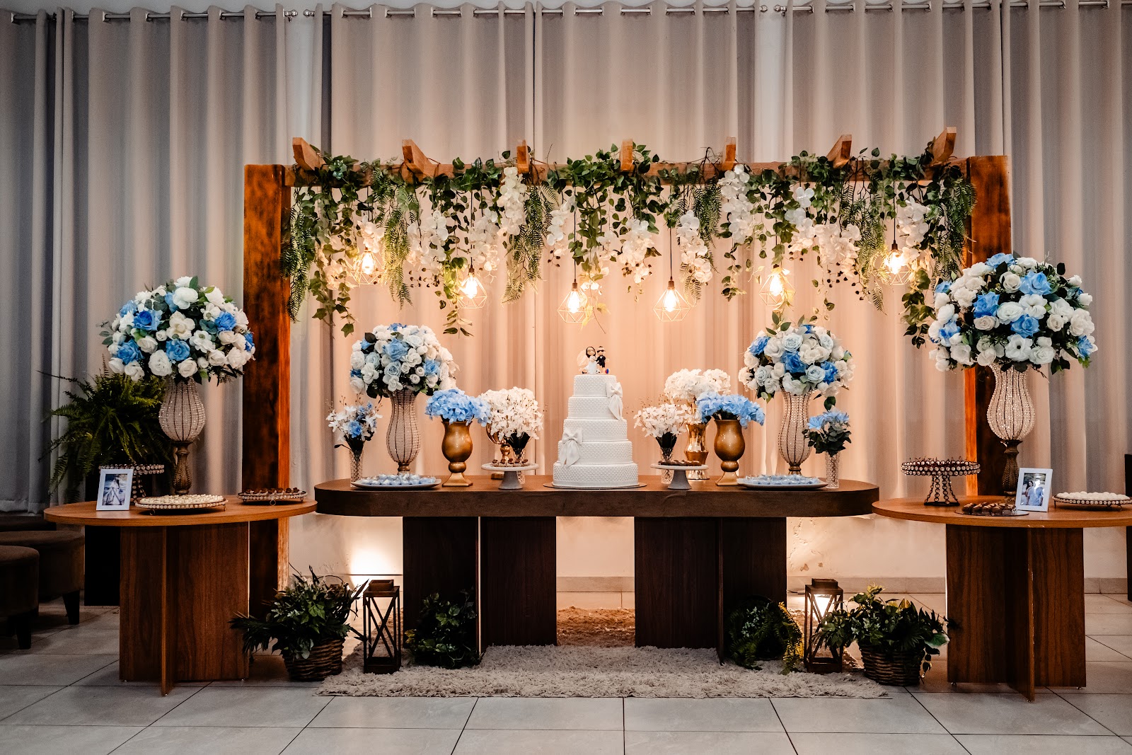 Mesa de honra do salão com painel de flores, cortinas e iluminação cênica
